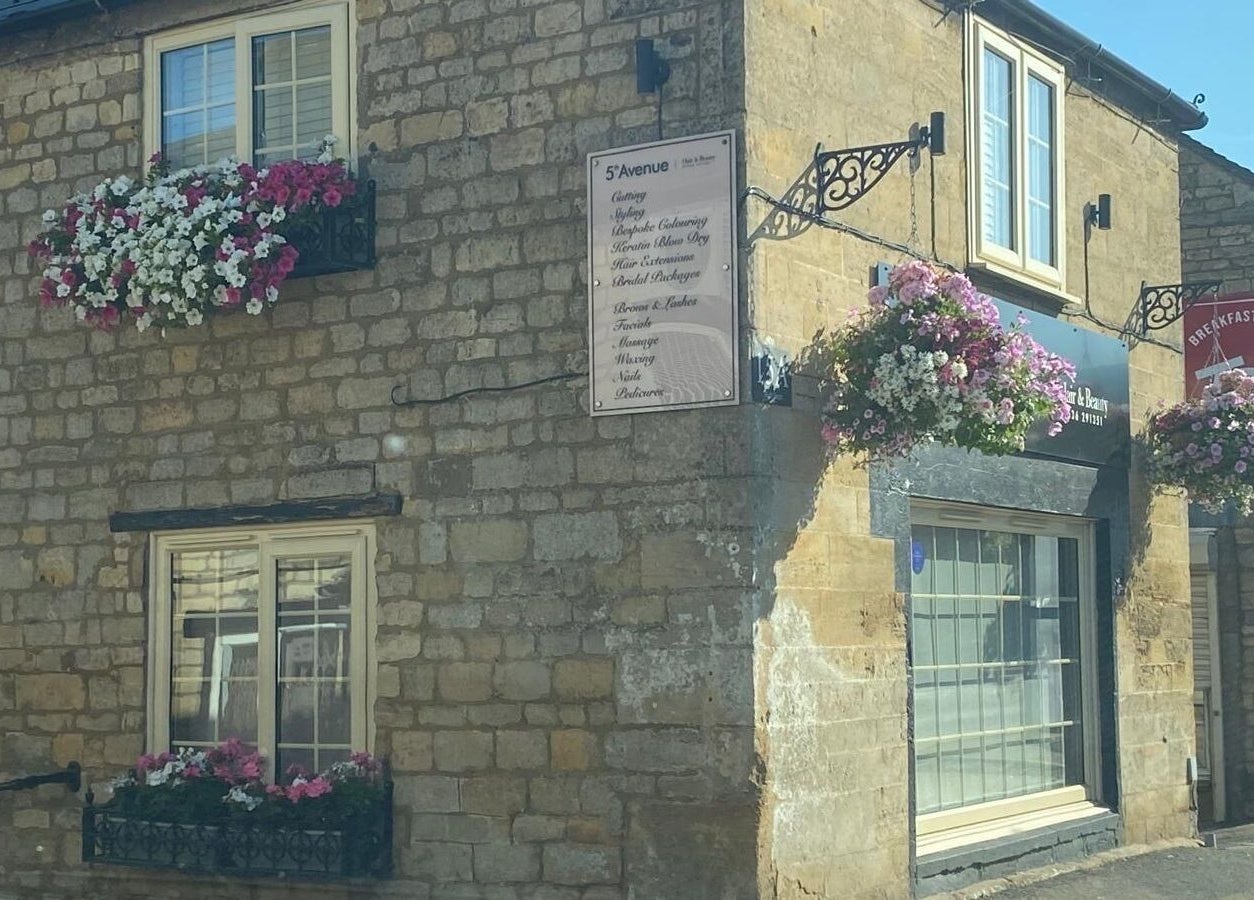Exterior of Be Happy Nails By Becca in Weldon, England, GB, featuring hanging flower baskets on stone walls.
