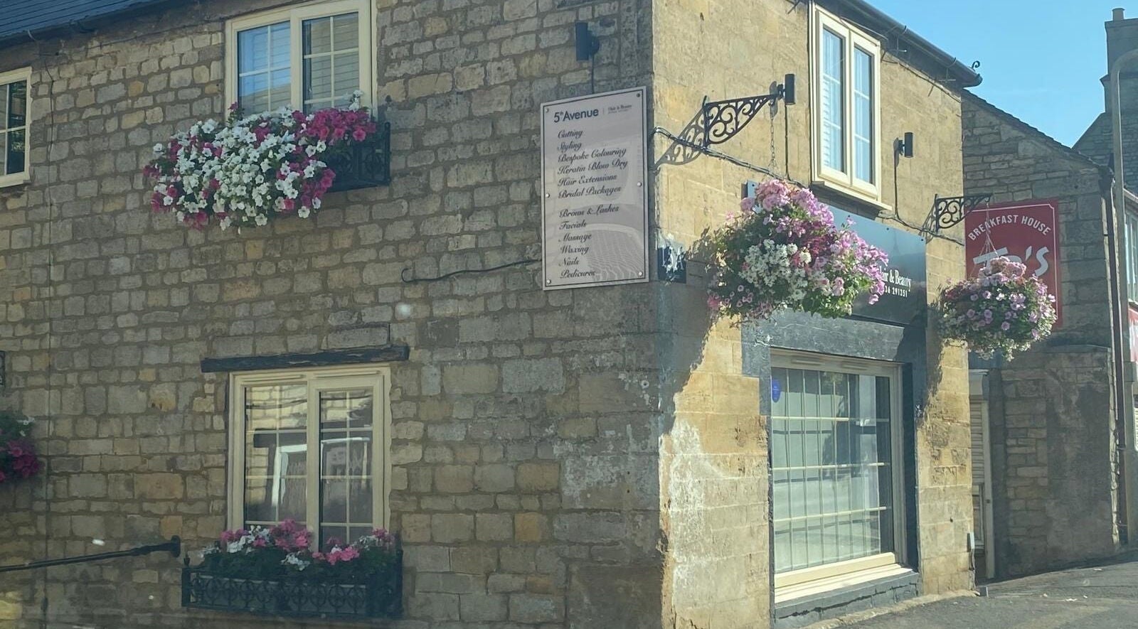 Exterior of Be Happy Nails By Becca in Weldon, England, GB, featuring hanging flower baskets on stone walls.