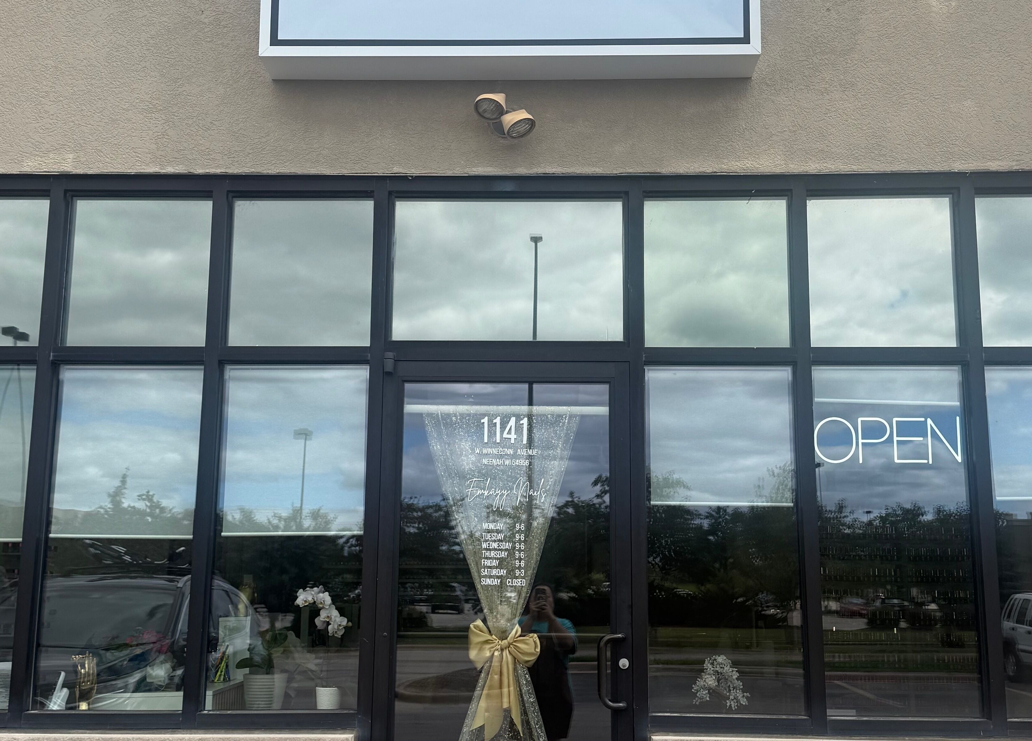 Front view of Emkayy Nails, Neenah, Wisconsin, US, with a welcoming open sign and elegant glass decor.