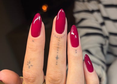 Stylish crimson nails with artistic tattoos at By Amelia Ldn, London, England, GB.