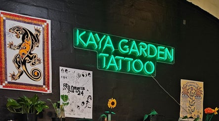 Neon sign at Kaya Garden Tattoo Haymarket, NSW, AU, surrounded by colorful tattoo posters and plants.