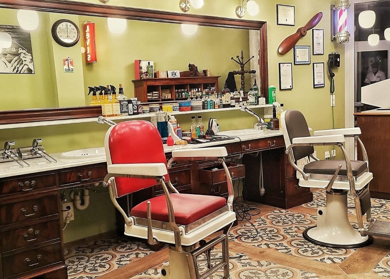 Interno elegante di Buddies Barbershop a Losone, Ticino, CH con poltrone vintage e specchio grandi.