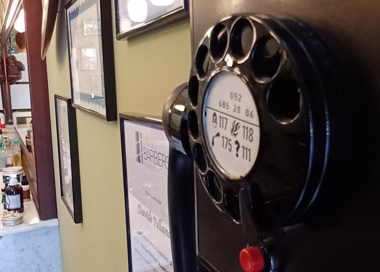 Interno vintage di Buddies Barbershop, Losone, Ticino, CH, con parete e oggetti classici.