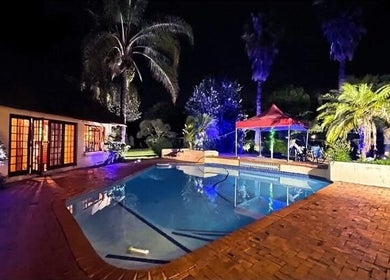 Omar Beauty Spa's poolside patio at night in Chartwell, Gauteng, ZA, featuring lit tropical gardens and tranquil ambiance.