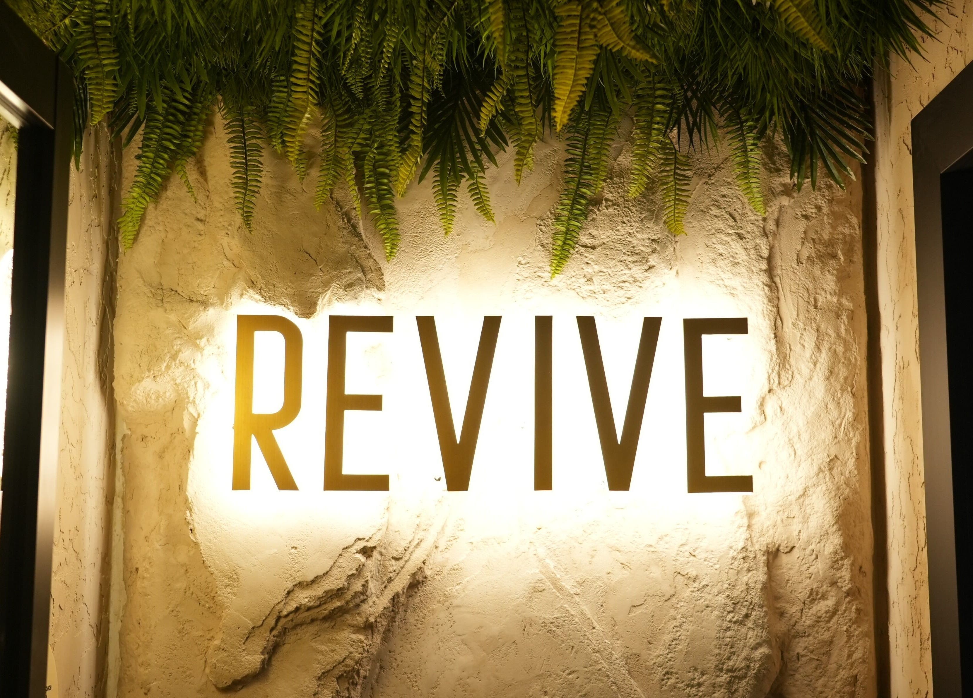 Illuminated REVIVE sign at REVIVE WELLNESS GLEBE, Glebe, New South Wales, AU, with lush greenery.