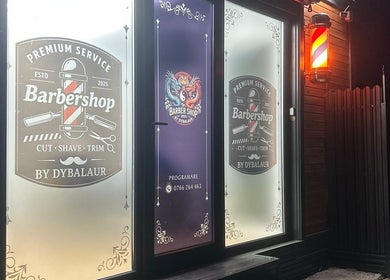 Ușa iluminată a Barber Shop DyBalaur, Măgurele, Județul Ilfov, RO, afișând logo-ul clasic al frizeriei.