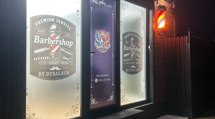 Ușa iluminată a Barber Shop DyBalaur, Măgurele, Județul Ilfov, RO, afișând logo-ul clasic al frizeriei.