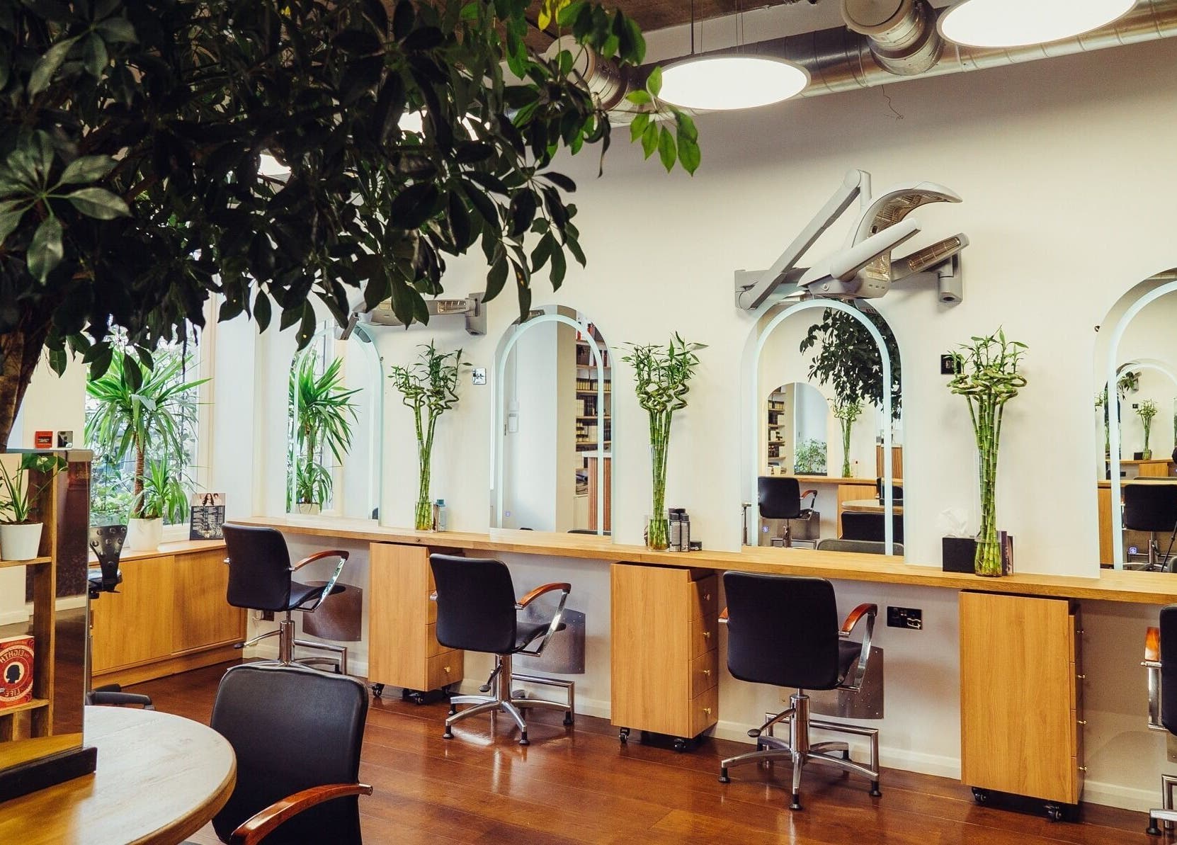 Bright, elegant salon chairs and mirrors at ADEM, London, England, GB, surrounded by lush greenery.