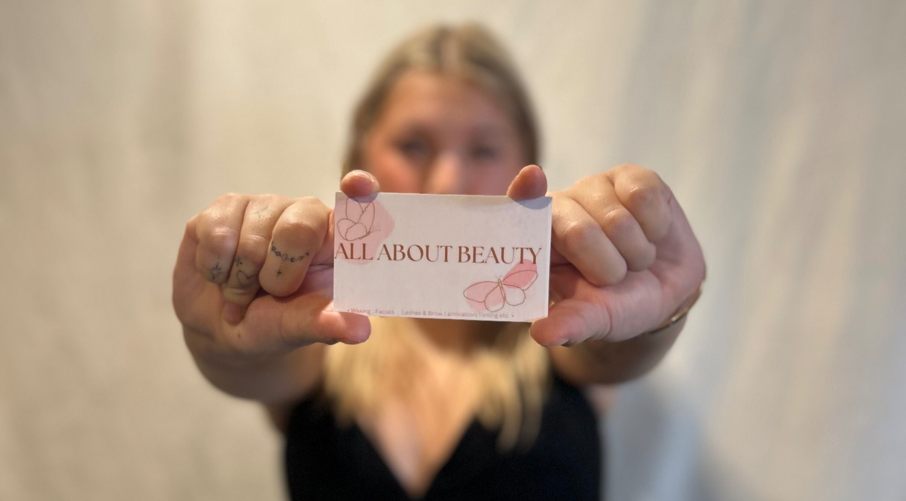 Close-up of hands holding an All About Beauty Salon LLC card in Eagan, Minnesota, US.
