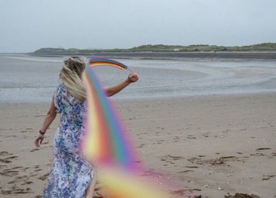 Woman with rainbow on beach at GC Therapies, Liverpool, England, GB. Serene sea and sandscape backdrop.