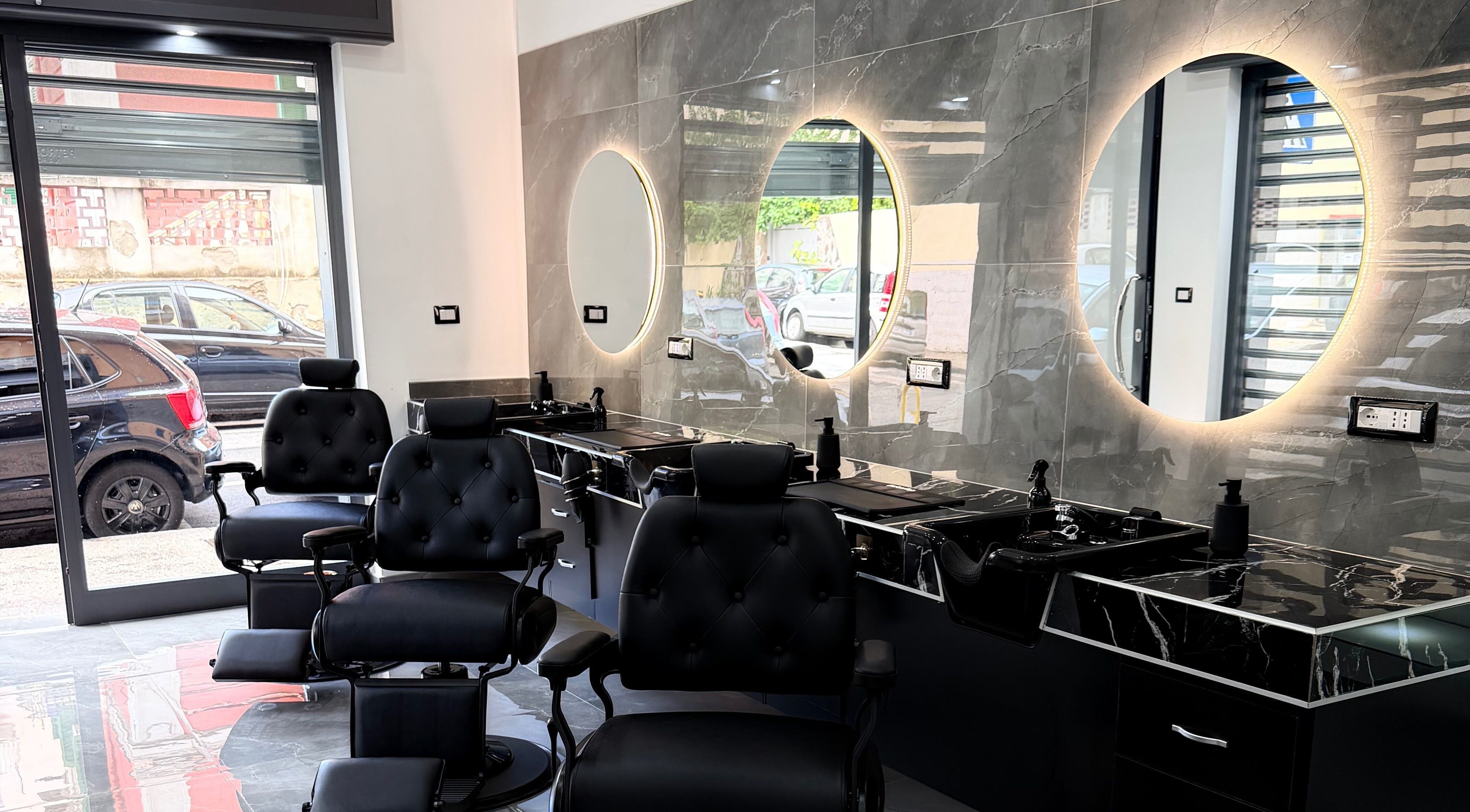 La moderna area di lavoro del GDP Barber Salon a Napoli, Campania, IT, con sedie e specchi illuminati.