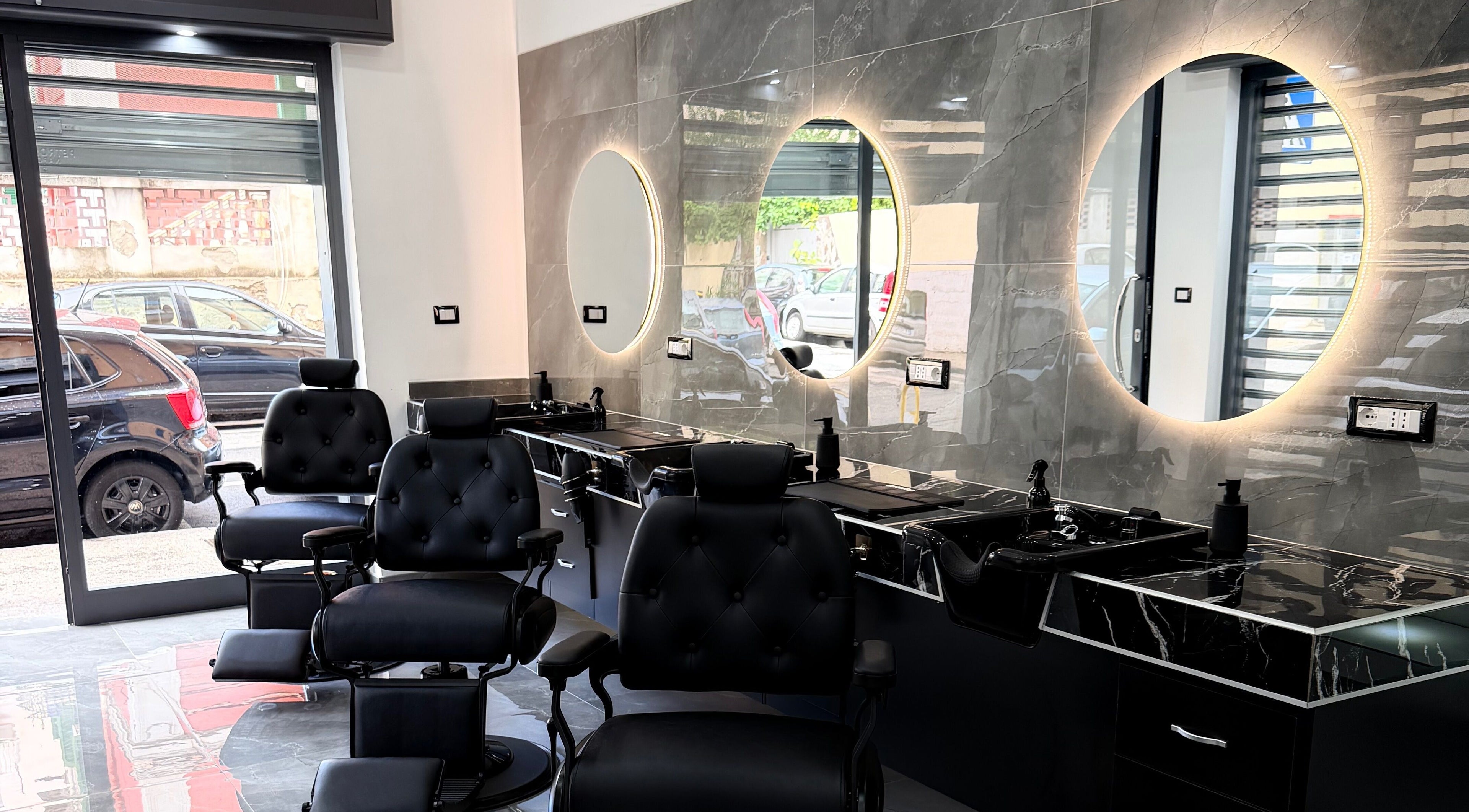 La moderna area di lavoro del GDP Barber Salon a Napoli, Campania, IT, con sedie e specchi illuminati.