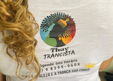 Detalhe da camiseta do Studio Thay Trancista, Rio De Janeiro, com cabelo loiro exuberante ao lado.