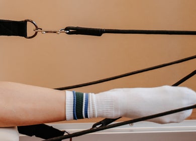 Pilates reformer in use at The Loft On Bowen, Waiuku, Auckland, NZ. A white socked foot engages with the equipment.