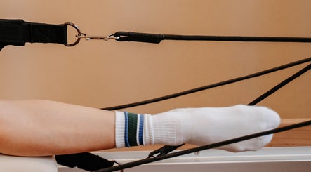 Pilates reformer in use at The Loft On Bowen, Waiuku, Auckland, NZ. A white socked foot engages with the equipment.