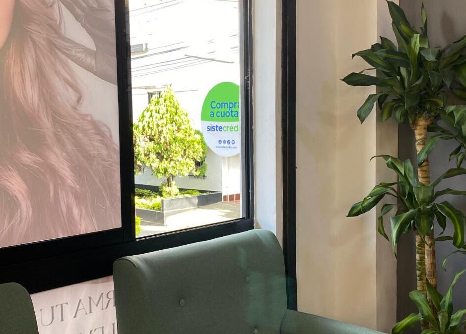 Área de espera en Elegance brows studio con plantas y sofá verde en Bello, Antioquia, CO.