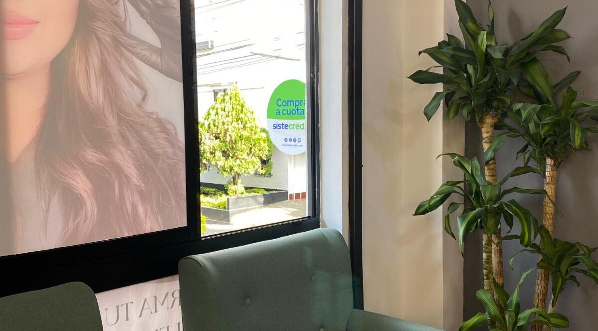 Área de espera en Elegance brows studio con plantas y sofá verde en Bello, Antioquia, CO.