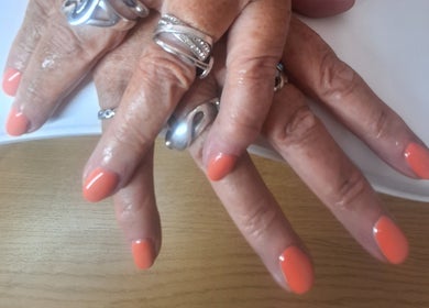 Polished and Pretty manicure with vibrant coral nails in Crynant, Wales, GB. Silver rings add elegance.