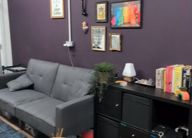 Cozy seating area at Shadow Bloom Studio, Oldham, England, GB with gray sofa and books on a shelf.