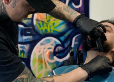 Expert providing a precise beard trim at Jonas Wayne, Norwalk, Connecticut, US, with colorful graffiti backdrop.