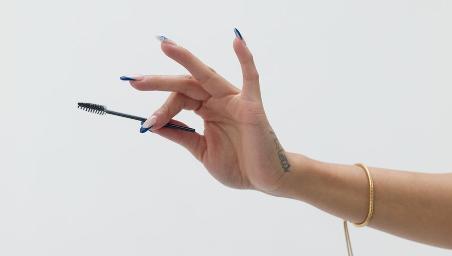 A hand with manicured nails holding a mascara wand at Mia Lashed, Brampton, Ontario, CA.