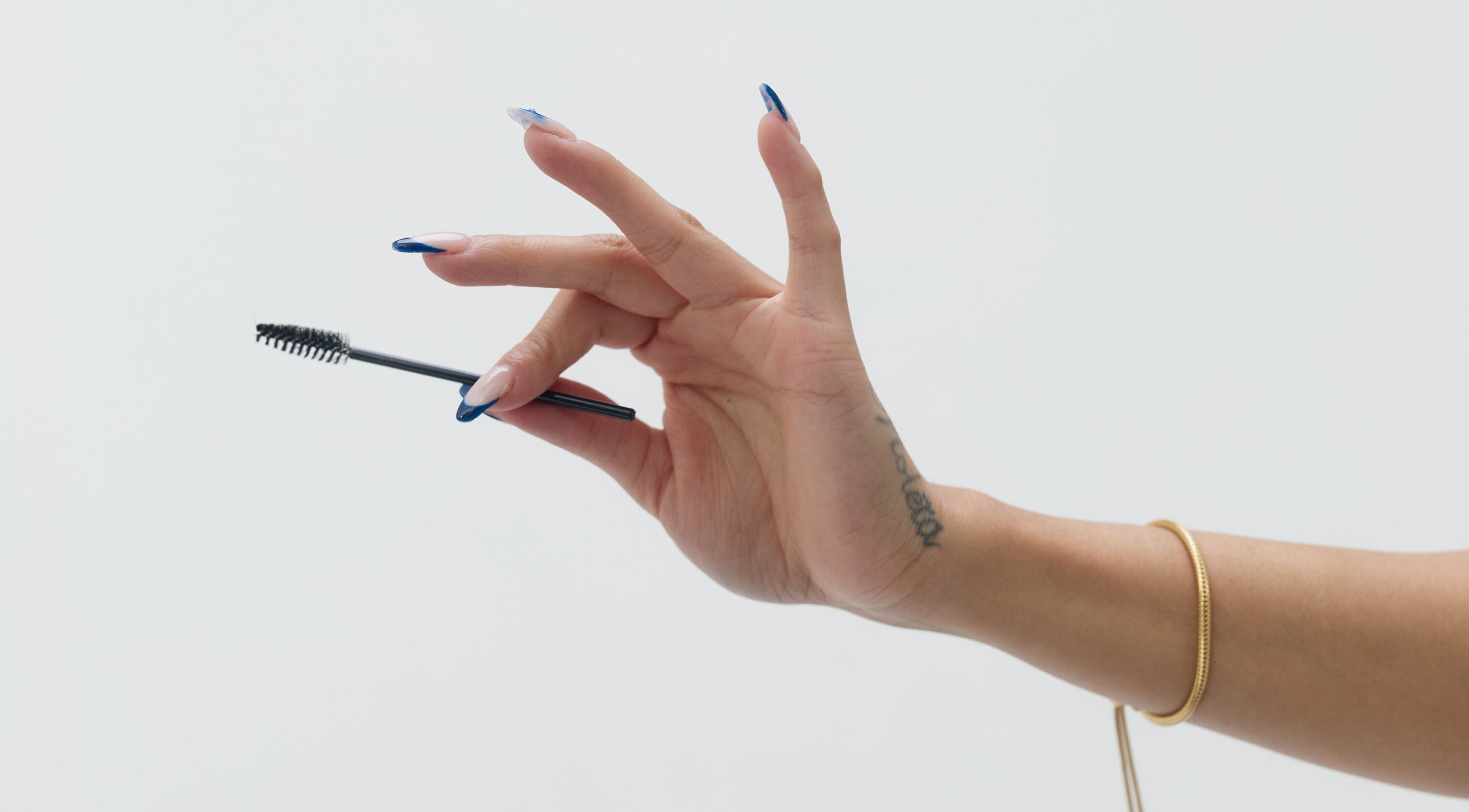 A hand with manicured nails holding a mascara wand at Mia Lashed, Brampton, Ontario, CA.