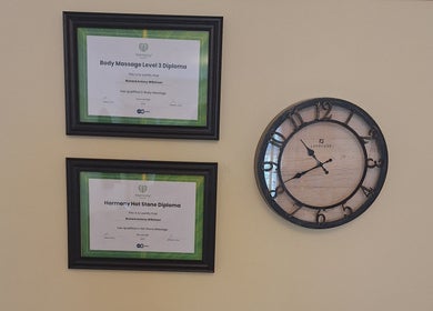 Diplomas and clock on cream wall at Calming-Massage in Blean, England, GB, symbolizing professionalism.