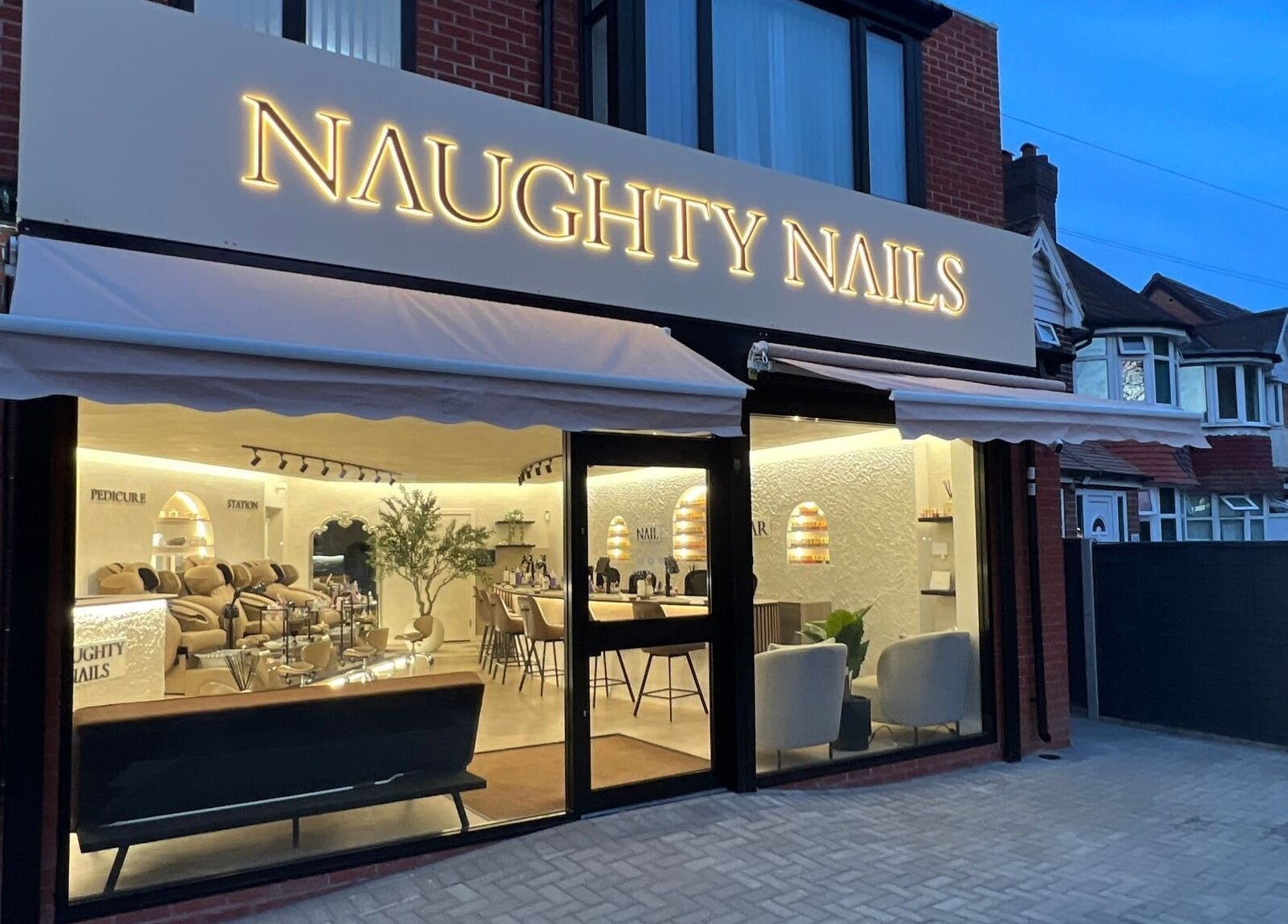 Exterior view of Naughty Nails salon in Birmingham, England, GB showcasing a stylish interior at twilight.