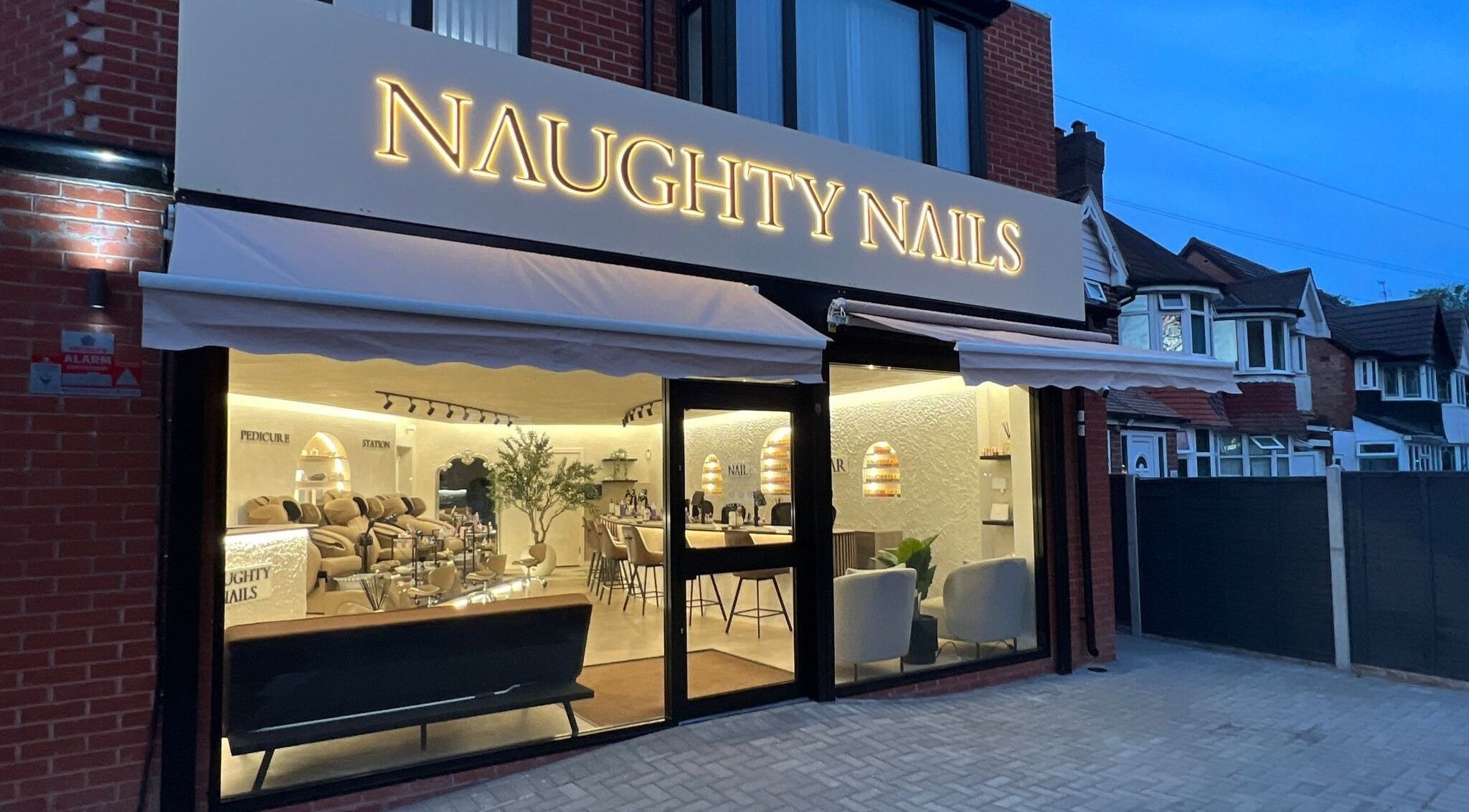 Exterior view of Naughty Nails salon in Birmingham, England, GB showcasing a stylish interior at twilight.