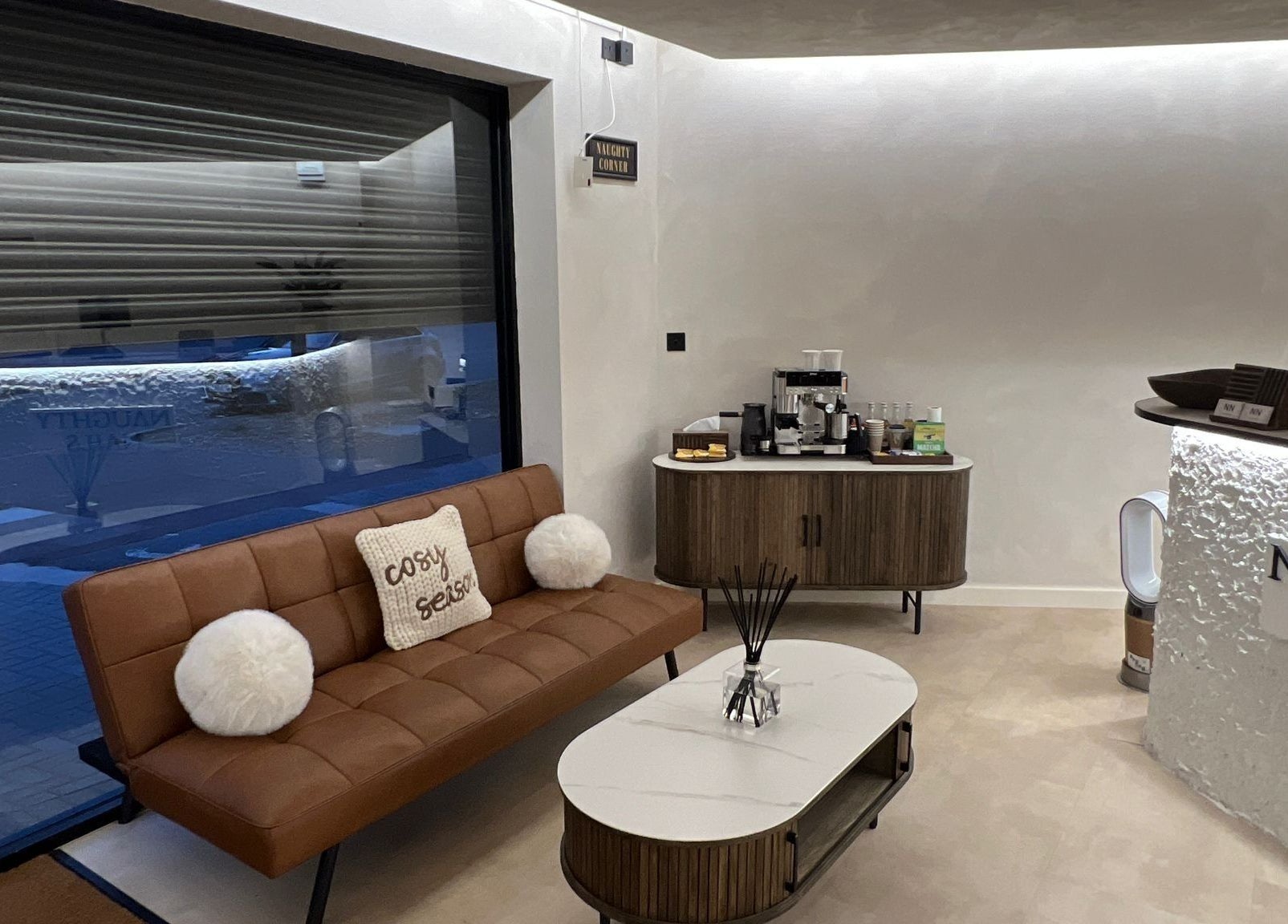 Cozy lounge area at Naughty Nails, Birmingham, England, GB featuring a sofa and coffee station.