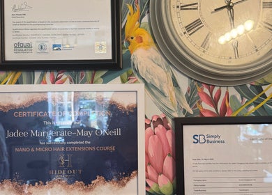 Elegant wall display at Jades Gorgeous Hair, Leighton Buzzard, with framed certificates and vibrant floral wallpaper.