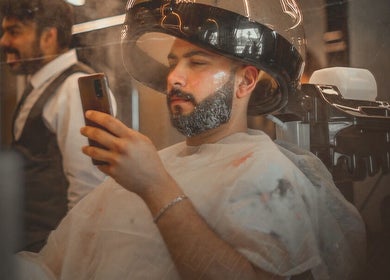 عميل يجلس تحت جهاز تجفيف الشعر في Shad's Men's Salon، القاهرة، يتمتع بخدمة وعناية فائقة.