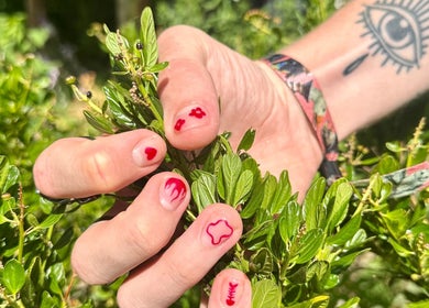 Hand met rode nagelkunst op groen blad bij Liberty City Nail Studio, Amersfoort, Utrecht, NL.