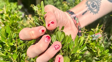 Hand met rode nagelkunst op groen blad bij Liberty City Nail Studio, Amersfoort, Utrecht, NL.