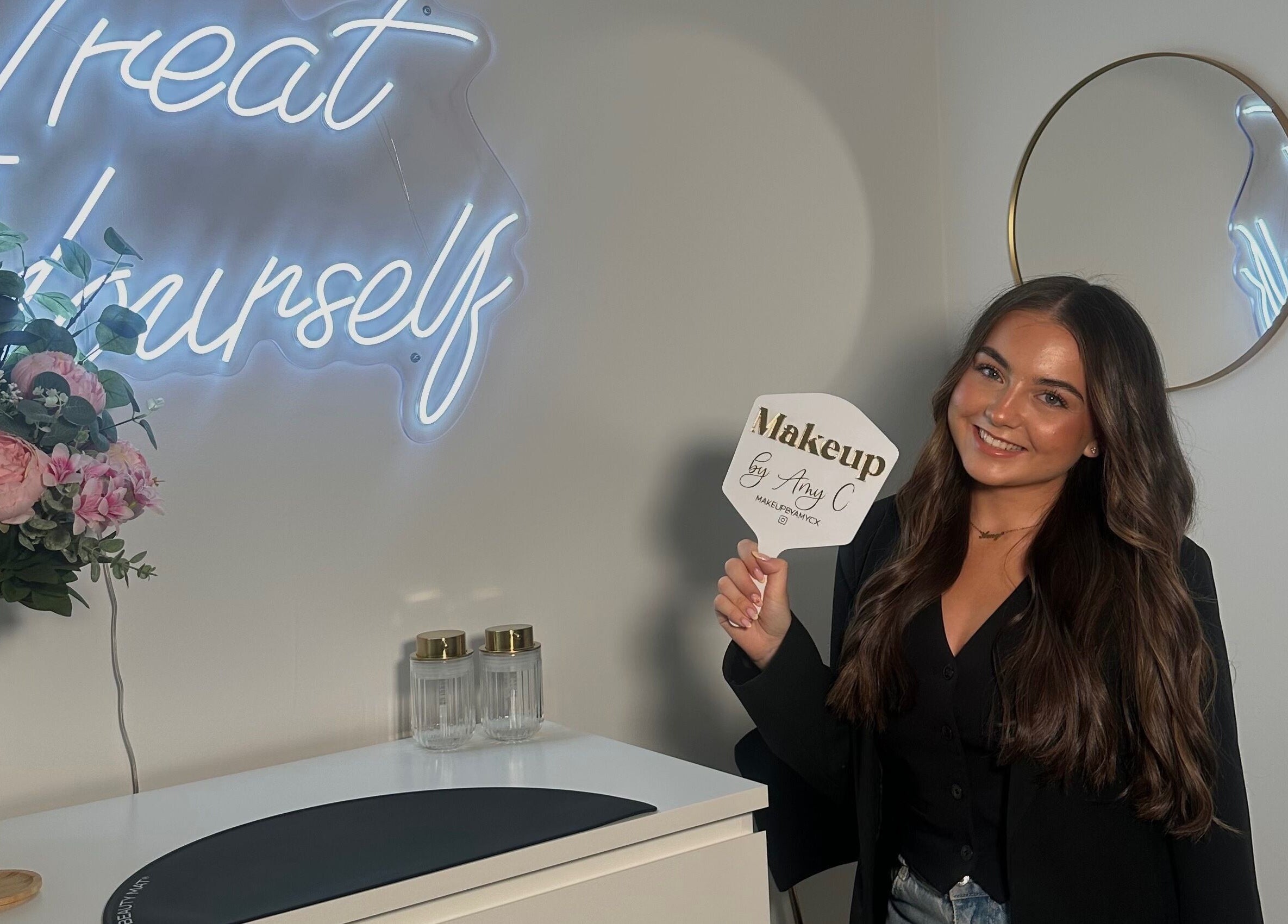 Inside MakeupbyAmyC in East Kilbride, Scotland; woman holds branded mirror, elegant decor visible.