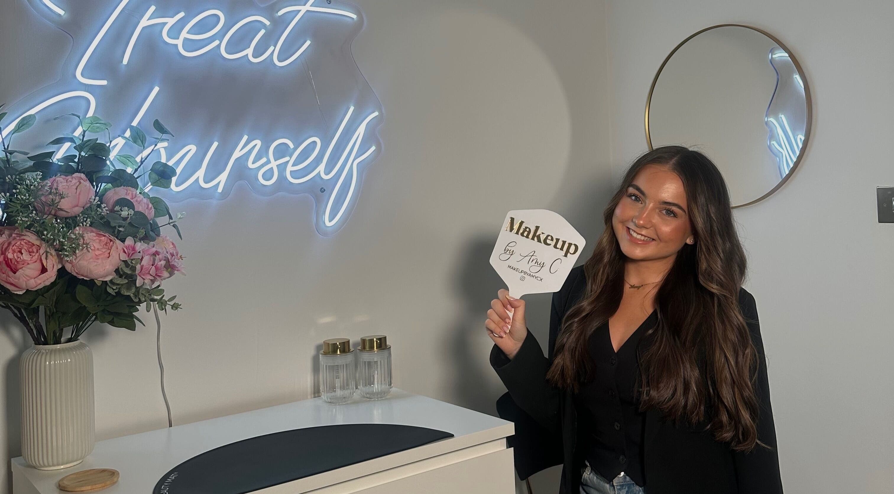Inside MakeupbyAmyC in East Kilbride, Scotland; woman holds branded mirror, elegant decor visible.