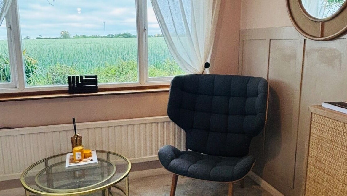 Cozy chair by window at Pristine Ink, Brentwood, England, GB, overlooking serene greenery.