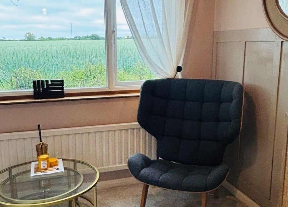 Cozy chair by window at Pristine Ink, Brentwood, England, GB, overlooking serene greenery.