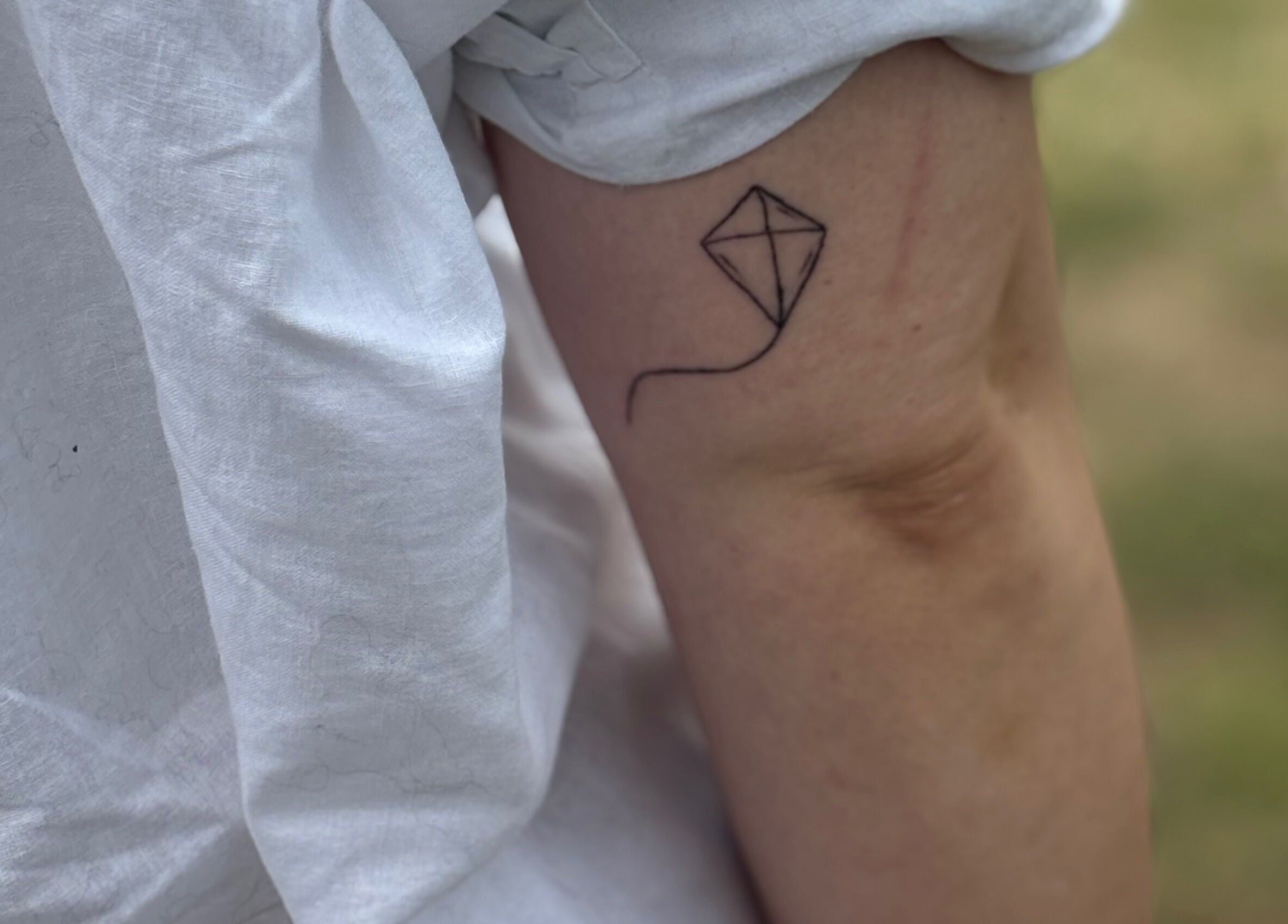 Minimal kite tattoo on arm at Pristine Ink, Brentwood, England, GB, showcasing fine line artistry.