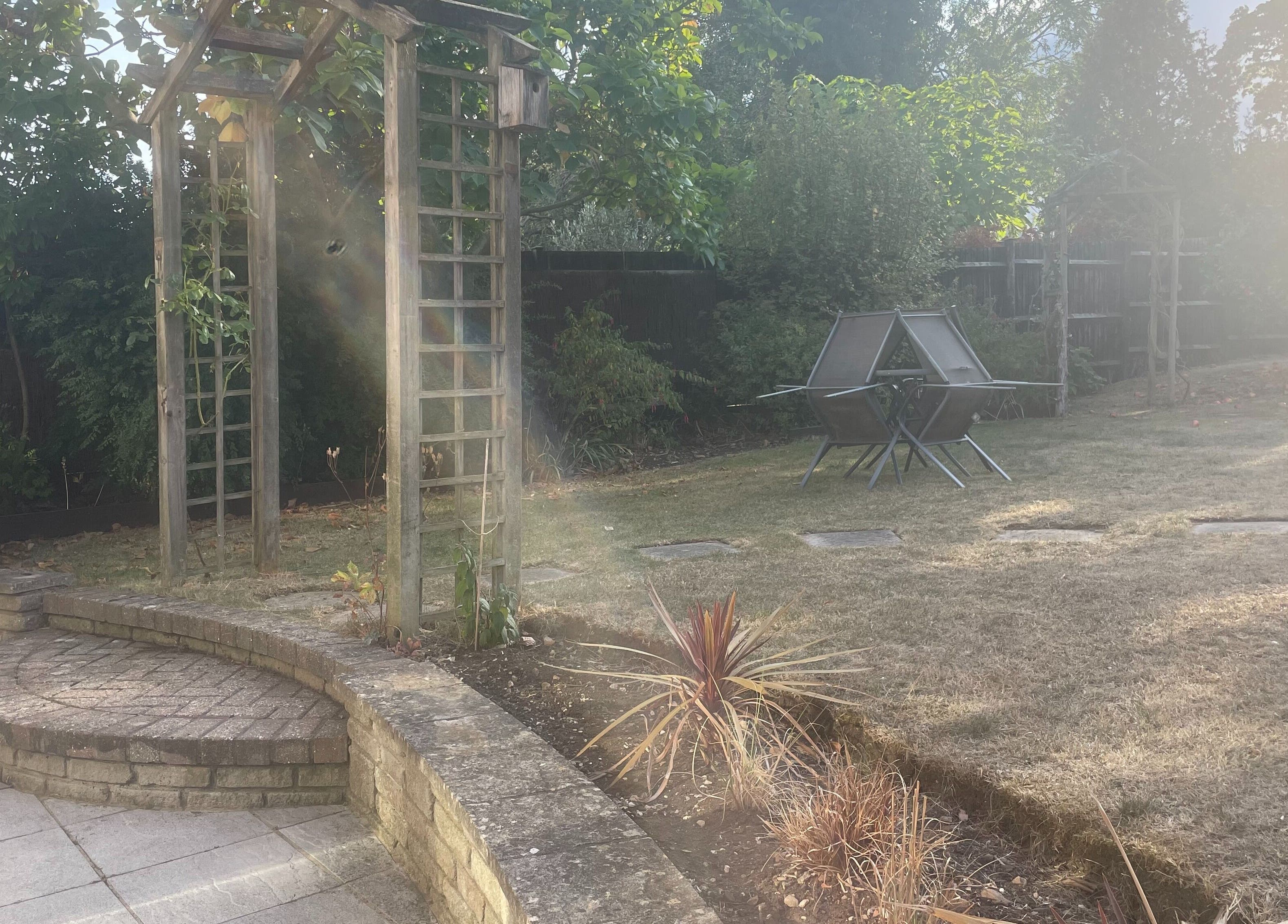 Serene garden at Temiluxe in Keynsham, England, GB, featuring a sunlit seating area and lush greenery.