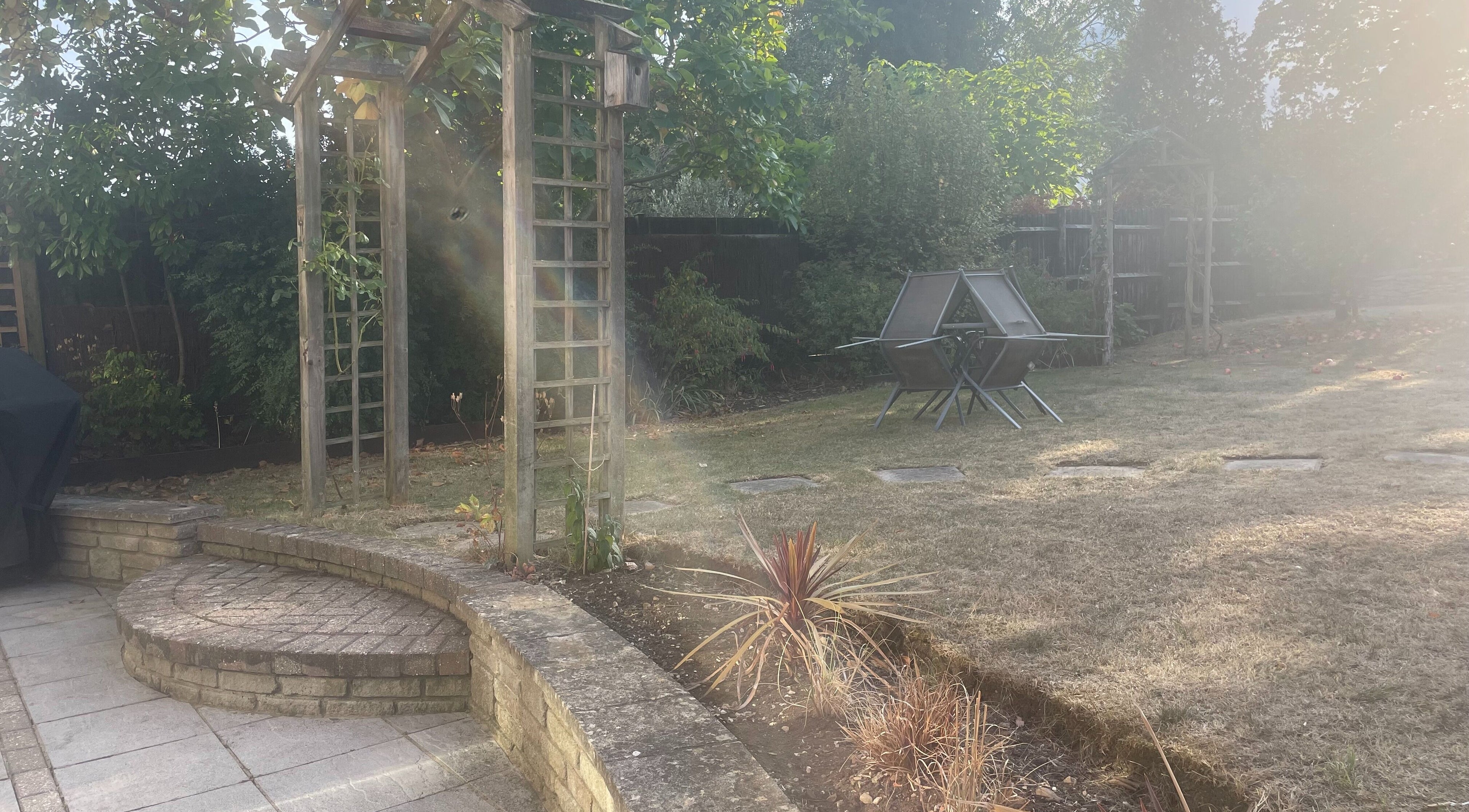 Serene garden at Temiluxe in Keynsham, England, GB, featuring a sunlit seating area and lush greenery.