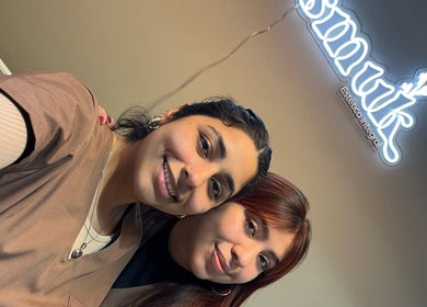 Dos profesionales sonríen en Smuk Nails, Córdoba, Córdoba, AR, iluminadas por un letrero brillante.