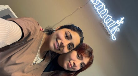 Dos profesionales sonríen en Smuk Nails, Córdoba, Córdoba, AR, iluminadas por un letrero brillante.