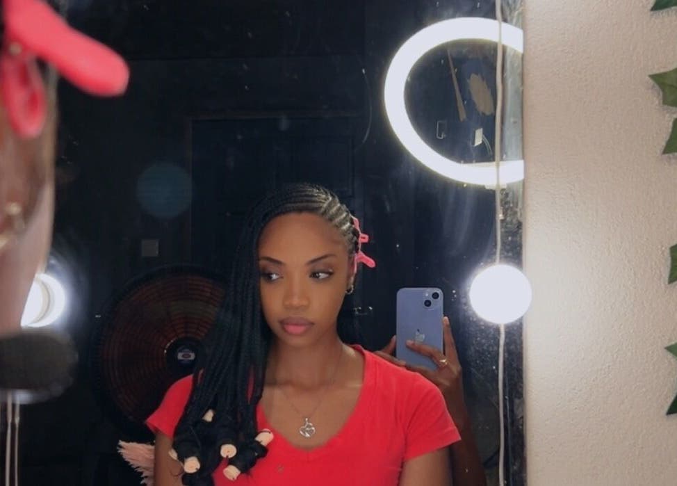 Woman with braids reflected in mirror at JusstBraids, Oistins, Christ Church, BB, showcasing vibrant hairstyle.