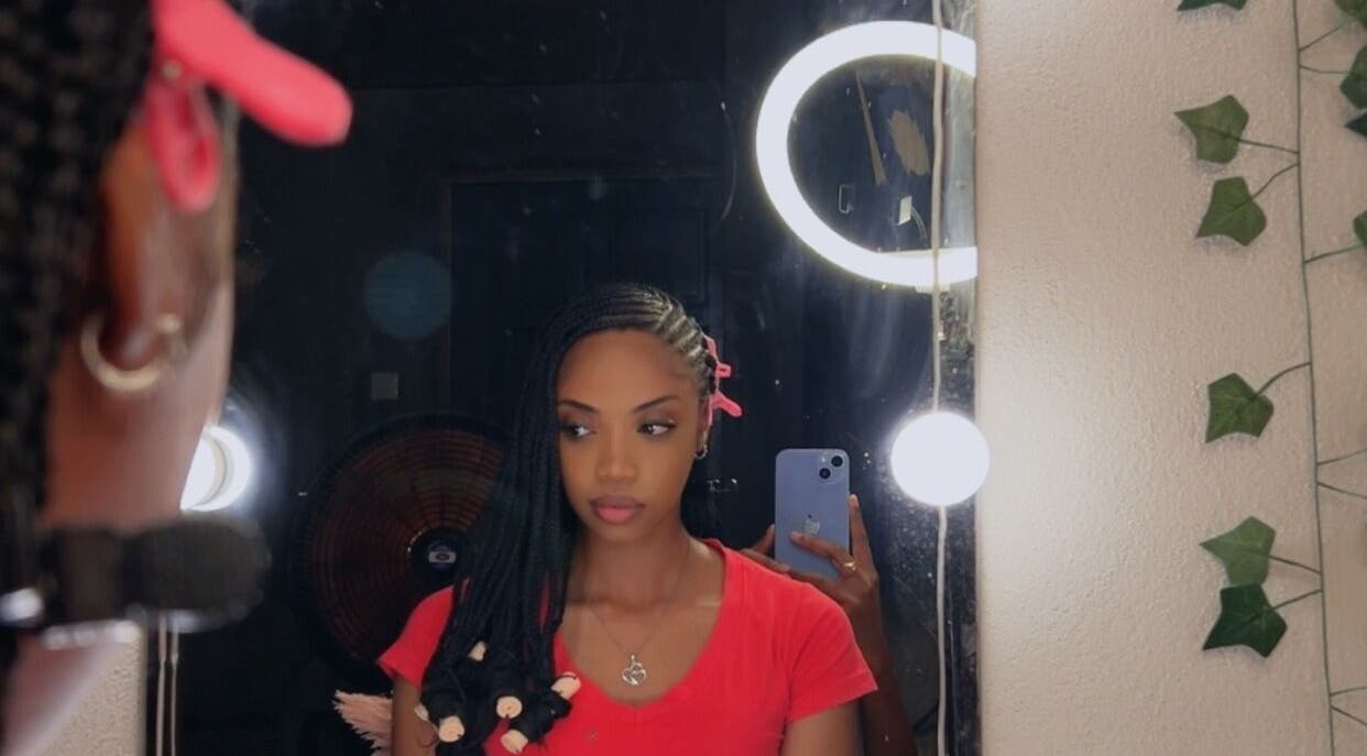Woman with braids reflected in mirror at JusstBraids, Oistins, Christ Church, BB, showcasing vibrant hairstyle.