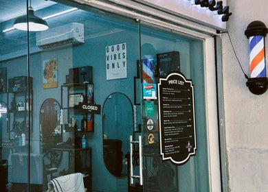 Entrance of Hombre Barbers (Tampines) in Singapore, SG, showcasing a modern interior with a price list on the glass door.