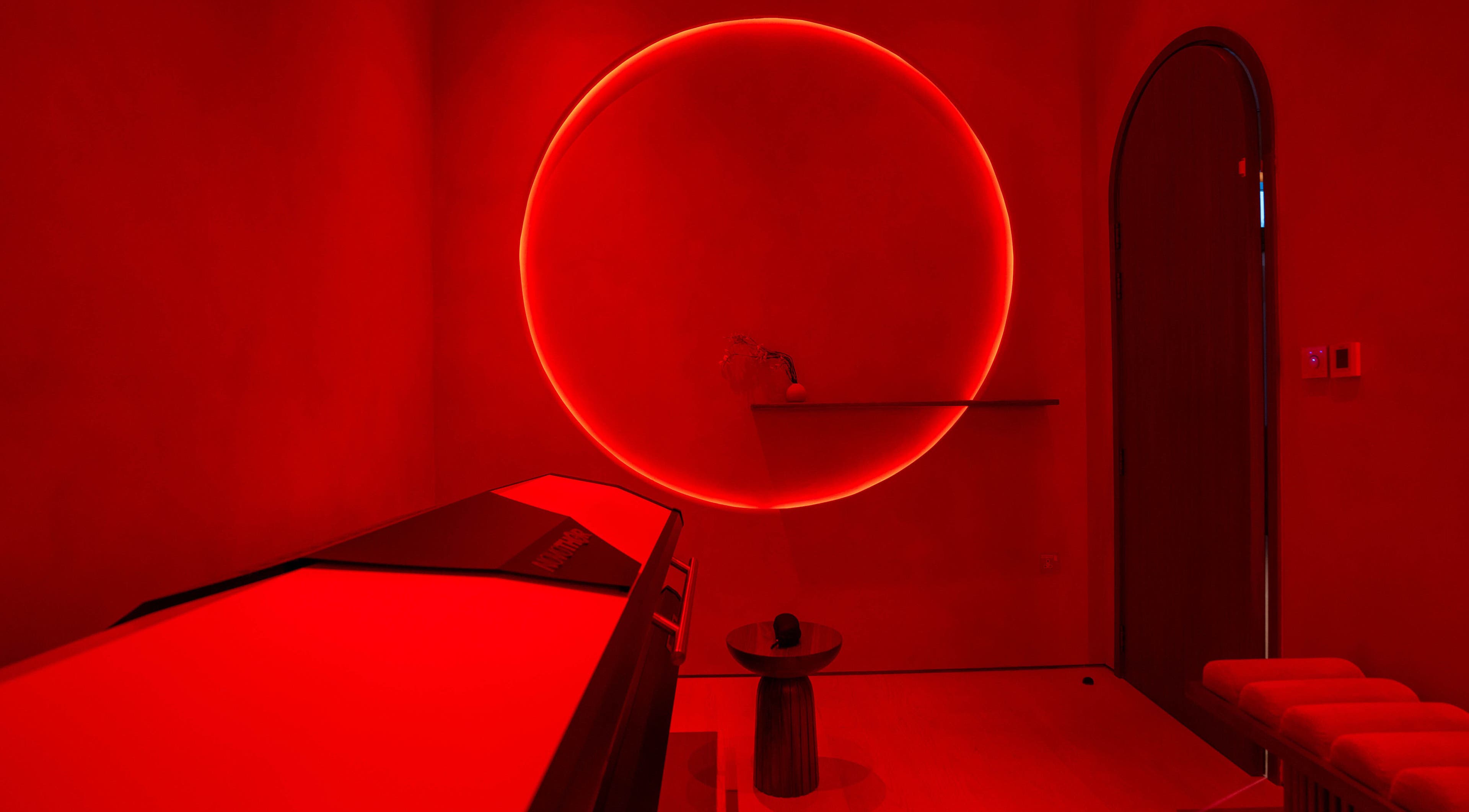 AKARI wellness room in District, دبي, AE, featuring a red-hued infrared therapy space with a glowing circle.