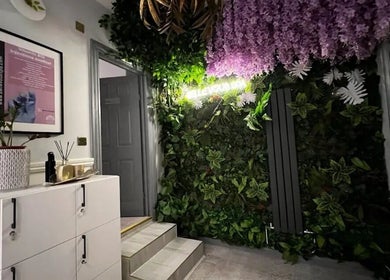 Green wall with purple flowers at PureLi Skin Clinic, London, England, GB, creating a serene entrance.