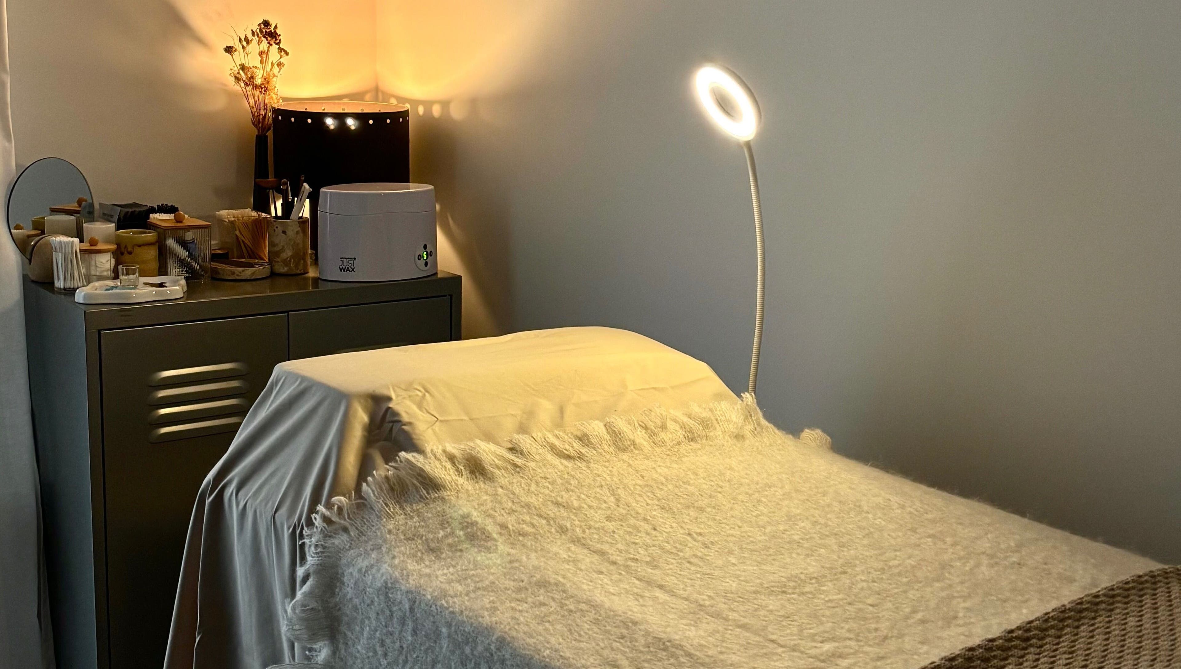 Cozy treatment bed in LAÙ Treatment Studio, Loughton, England, GB, with warm lighting and beauty products.