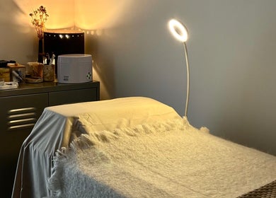 Cozy treatment bed in LAÙ Treatment Studio, Loughton, England, GB, with warm lighting and beauty products.